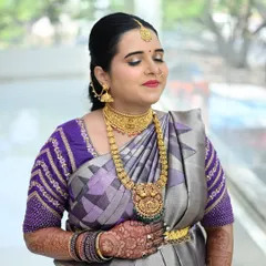 A close-up of the gorgeous mom-to-be, Sahana. Her makeup features soft, glowing skin and a bright lip, perfectly complementing her purple and silver silk saree and traditional gold jewelry.