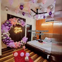 An elaborate and romantic birthday room decoration. This setup includes a full balloon ring in purple and pink, balloons on the ceiling, and a path of rose petals leading to the bed.