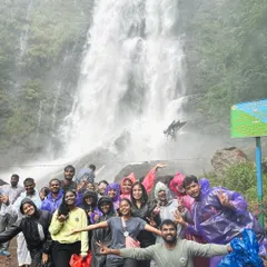 A joyful group in raincoats posing in front of a gushing monsoon waterfall. My trips are designed to make the most of the rainy season's spectacular sights.