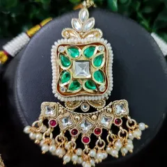 A macro shot of a necklace pendant, showcasing the square green stones and surrounding kundan work.