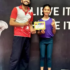 This young gymnast proudly displays her achievement certificate alongside her coach.