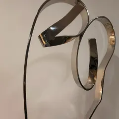 A close-up of "The Bond," a sculpture representing the love between a mother and child. The flowing lines of stainless steel create an abstract figural form that is both strong and tender.