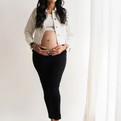 A simple and beautiful portrait. The mom-to-be is wearing a casual white jacket and black pants, creating a clean and modern look. The soft light from the studio window gives her a lovely glow.