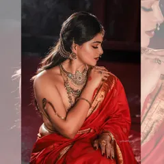 A modern take on a classic pose, this image emphasizes the beautiful lines of the backless blouse and the elegant drape of the red silk saree. The lighting is soft yet dramatic, highlighting the bride's profile and the antique jewelry.
