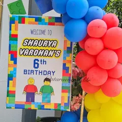 A personalized welcome sign for Shaurya's 6th birthday, featuring a LEGO block border and characters, framed by a primary-colored balloon garland.