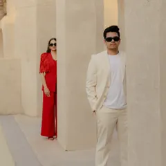 A stylish, modern portrait set against the minimalist architecture of the Dubai desert. The bold red and clean white outfits create a stunning contrast, showcasing how we blend high fashion with intimate storytelling.