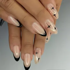 A modern twist on the classic French manicure. This design features sharp, black French tips on a clean, natural base, accented with minimalist black starbursts and a sprinkle of glitter for a chic and edgy look on almond-shaped nails.