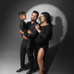 Celebrating the journey to parenthood with a classic, dramatic studio portrait. This maternity session uses a spotlight effect and coordinated black outfits to create a sophisticated and timeless family photograph.