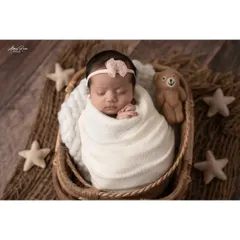 A beautiful overhead shot of a sleeping baby girl, snugly wrapped in a basket. The rustic textures of the basket and mat contrast beautifully with the soft white wrap and fabric stars, creating a lovely composition.