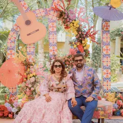 The happy couple seated at their Mexican-themed Mehendi. The backdrop features colorful florals, patterned tiles, and a guitar prop, perfectly complementing their festive outfits.