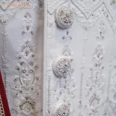Attention to detail is everything in bespoke tailoring. This close-up shows the custom-made, fabric-covered buttons on an all-white wedding sherwani, each intricately embroidered to match the garment's delicate patterns. It’s these small touches that create a truly royal look.