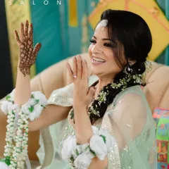 A radiant and happy bride during her Haldi ceremony. The makeup is minimal and fresh, with a focus on glowing skin, a simple bindi, and a touch of color on the lips. The braided hairstyle with fresh flowers completes this joyful pre-wedding look.