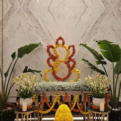 A full view of the festive Ganesh decor against a marble wall. The symmetrical arrangement, with offerings made of yellow and red flowers, creates a serene and beautiful focal point perfect for a corporate or hotel lobby.