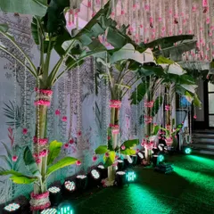 A close-up of the entrance decor for the pink and white Janoi ceremony. Traditional banana trees are adorned with delicate strings of white and pink flowers, blending natural elements with a soft, elegant color scheme.