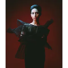 A striking portrait of model Athena against a bold red background. The architectural black garment and clean makeup create a powerful, high-fashion image that is both modern and timeless.