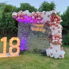 An outdoor 18th birthday party with a silver sequin wall. The rose gold and white balloon arch and large marquee numbers create a stunning evening look.