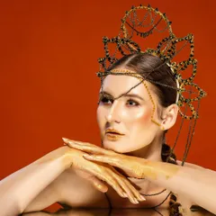 A creative portrait of a model with gold-painted hands and an intricate headpiece. We love collaborating on artistic projects that explore unique makeup, styling, and lighting techniques.