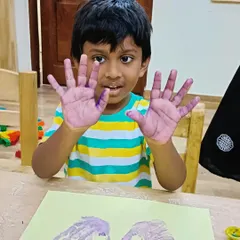 A young boy shows his purple painted hands, ready for an art project. We love capturing these simple, joyful moments.