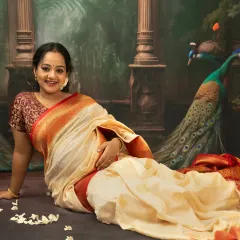 A graceful pose on the floor, allowing the beautiful silk saree to flow naturally. This shot captures the mother's happy expression, surrounded by traditional elements like a brass diya and flower petals.