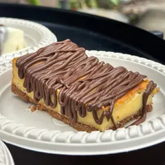 A close-up of our classic baked cheesecake, drizzled generously with Nutella. The golden-baked surface and creamy interior make this a timeless favorite.