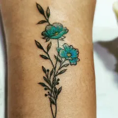A close-up of a delicate floral tattoo. I used a mix of fine black lines for the stem and leaves, with a pop of turquoise blue for the flowers to create a beautiful contrast.