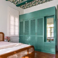 This bedroom features a stunning teal wardrobe with louvered doors and an integrated dressing mirror. The design is paired with a leaf-patterned wallpaper on the ceiling for a touch of tropical drama.