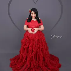 A beautiful studio portrait in a red ruffled gown. The heart-shaped hand gesture on the baby bump adds a sweet, symbolic touch.
