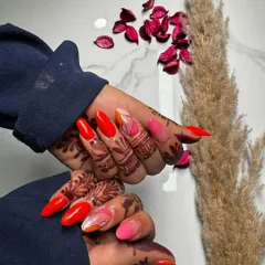 Bright and beautiful nails to complement intricate henna designs. This set features sharp, stiletto-shaped extensions with a mix of vibrant red and pink shades.