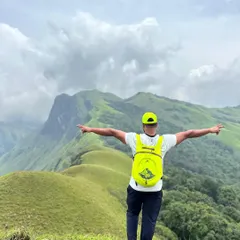 A trekker soaking in the vast expanse of the Netravati landscape. The bright backpack stands out against the endless green hills of Chikmagalur.