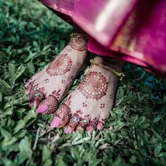 A creative shot focusing on the bride's feet, adorned with beautiful mehndi and traditional toe rings. The contrast with the green grass makes the details pop.