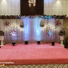 This stage design for a wedding event uses a combination of white drapes, hanging floral baskets, and blue uplighting for a cool, elegant effect. The setup is perfect for an indoor banquet hall and provides a beautiful backdrop for photos.