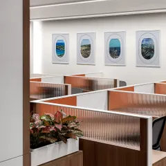The main office area of 'The High-Flying Office' features workstations with fluted glass partitions and airplane window-inspired artwork. This design choice reinforces the aviation theme of the TajSATS brand while maintaining a sense of openness.