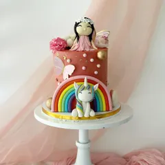 Another enchanting unicorn and fairy cake, this time with a terracotta-colored buttercream. The cake is adorned with a rainbow, a unicorn, a fairy, and gold sphere accents.