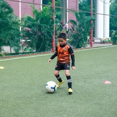 A young player practicing his dribbling skills around cones. We use age-appropriate drills to develop coordination and technique from the very beginning.