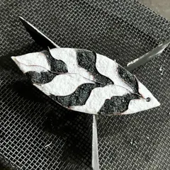 An enamel piece during the firing process, resting on a mesh before going into the kiln where the glass powder melts and fuses to the copper.