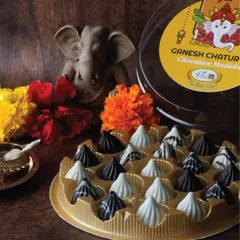 A tray of our assorted chocolate modaks set against a traditional puja backdrop with marigold flowers and a diya. This captures the essence of offering a modern, yet reverent, treat during the festival.