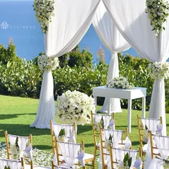 An elegant and minimalist white mandap setup for a seaside wedding. The clean lines and white floral arrangements draw attention to the stunning ocean view, creating a serene and picturesque ceremony space.