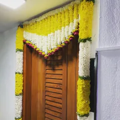 A simple yet beautiful floral decoration for a doorway. Garlands of yellow and white flowers frame the entrance, adding a touch of festive color for a puja or housewarming.
