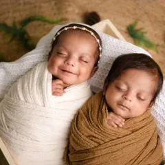 Two little peas in a pod. These twin babies are sleeping side-by-side in a wooden box, one in a white swaddle and the other in brown, creating a beautiful, earthy portrait.