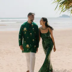 A beautiful, sun-drenched moment on a Sri Lankan beach. The couple walks hand-in-hand, their vibrant green outfits complementing the tropical setting, capturing the relaxed elegance of a destination wedding.