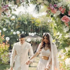 A happy couple walks hand-in-hand through a garden path framed by a beautiful arch of pastel roses.