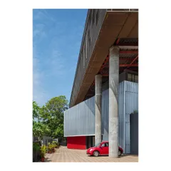 The "Hoverspace" office extension is supported by massive concrete columns, allowing the new volume to float above the ground. A red car provides a pop of color and a sense of scale.