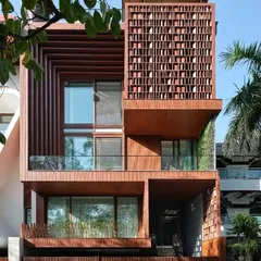 The 'Vrinda' residence features an intricate wooden jaali screen on its facade. This element provides privacy and shade while casting beautiful patterns of light, blending traditional Indian craftsmanship with contemporary design.