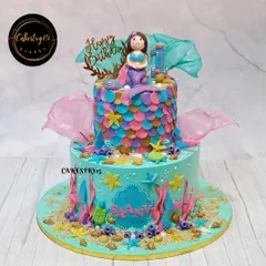 We created this vibrant two-tier mermaid cake for a first birthday celebration. It features colorful fondant fish scales, an underwater scene with coral and starfish, and a beautifully crafted mermaid topper.