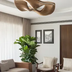 Lighting is more than just illumination; it's the jewelry of a room. This sculptural wooden chandelier in the West Coast Residence serves as a central art piece, anchoring the living space with its organic form and warm, ambient glow.