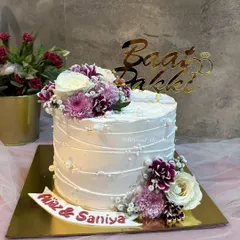 A sweet beginning for Aijaz and Saniya. This single-tier Baat Pakki cake features a textured white frosting, a beautiful arrangement of fresh flowers, and a custom gold topper to mark the special occasion.