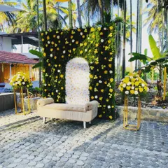 For this outdoor haldi ceremony, I created a vibrant photo spot with a lush greenery wall dotted with yellow and white flowers. The design includes a comfortable seating area and matching floral stands, all set against a beautiful natural backdrop of palm trees.