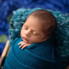 A close up shot of a baby boy nestled in a basket. The rich blue tones of the wrap and the fluffy texture of the liner create a beautiful, cozy image.