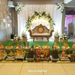 An elegant white and green theme for a Half-Saree ceremony. The stage features a beautiful arch of white gerberas, a classic sofa, and a stunning display of traditional platters.