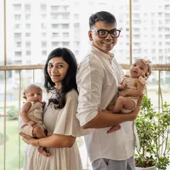A modern family portrait with newborn twins. This photo, taken on a balcony with natural light, feels fresh, authentic, and full of love.